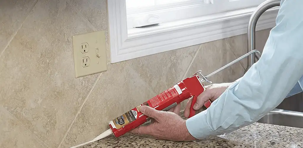Handyman applying caulk along a kitchen backsplash and countertop seam in Aurora, IL